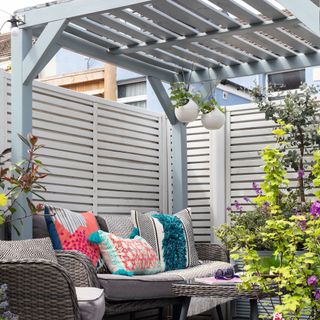 Light blue grey painted pergola with hanging plants and patterned outdoor sofa cushions