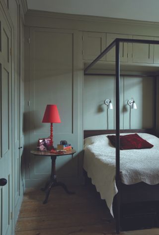 A bedroom in sage green colors, with a red lamp