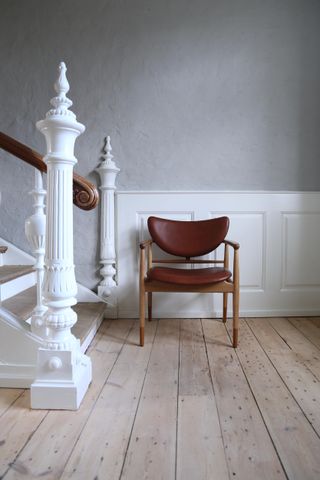 grey hallway with stripped back wooden floors, regal white banisters and a solo wood and leather chair at the foot of the stairs
