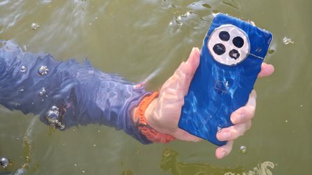Holding the blue OnePlus 13 under water in a lake