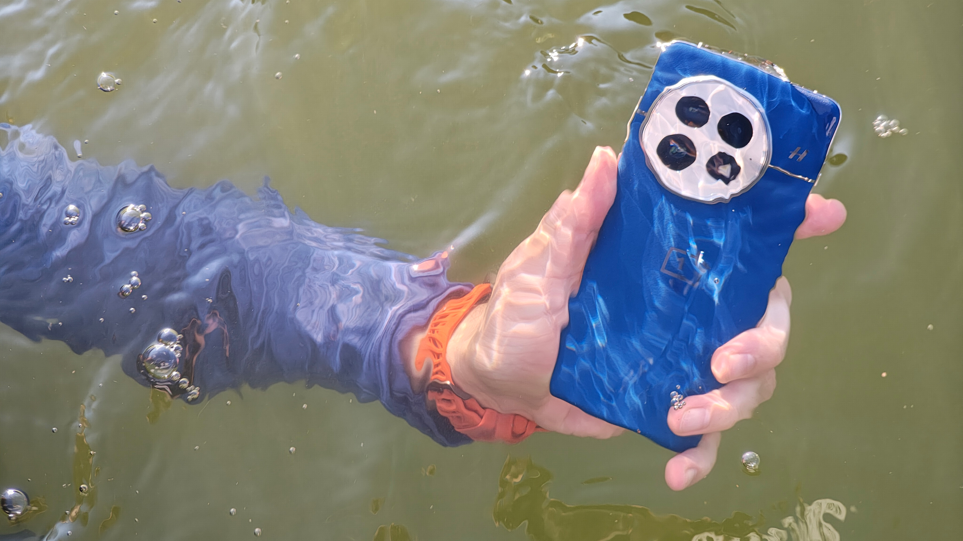 Holding the blue OnePlus 13 under water in a lake
