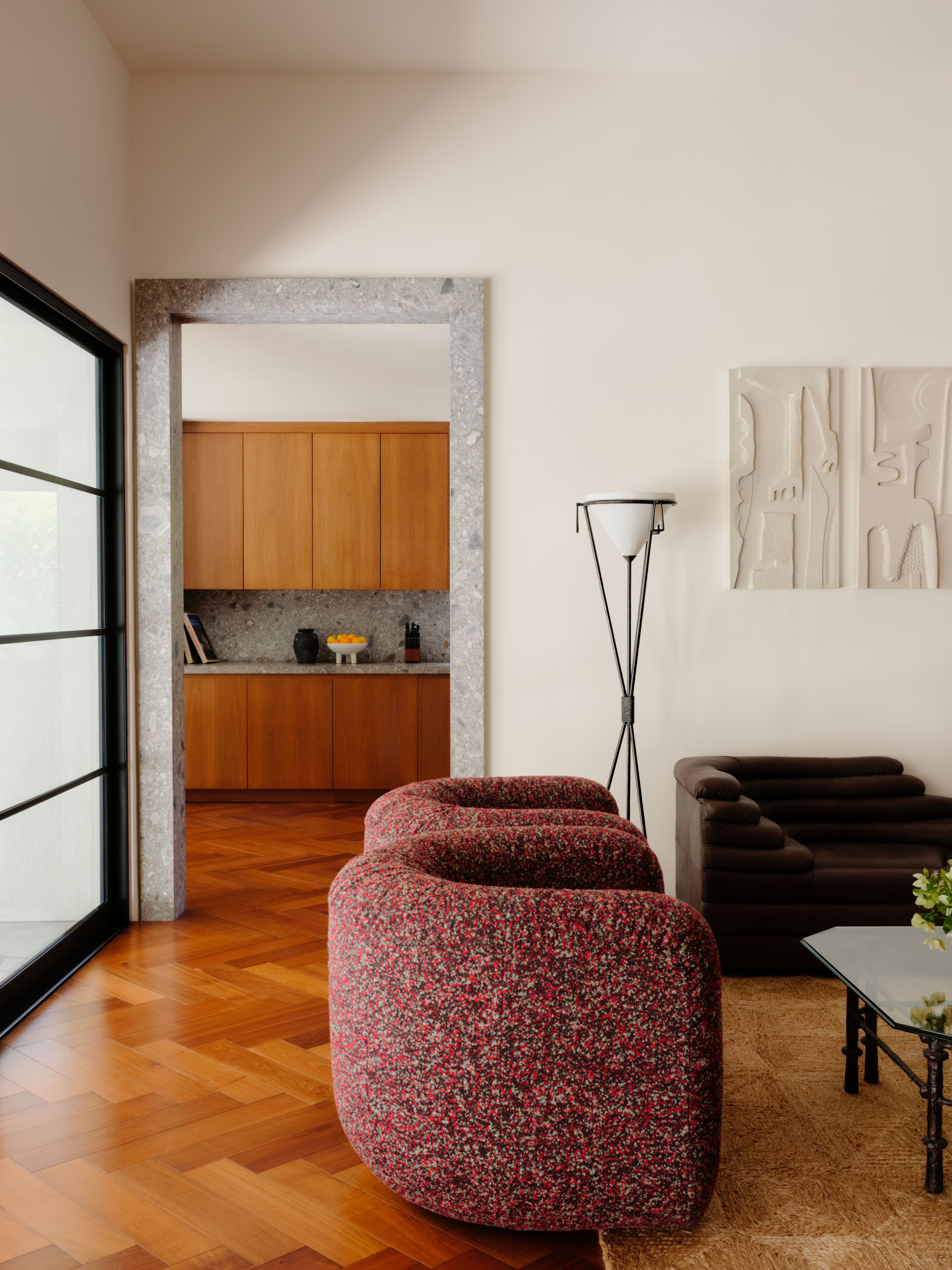 View from living room into the kitchen, both decked with shiny wooden floors, and elegant furniture, including sherling bordeaux armchairs.