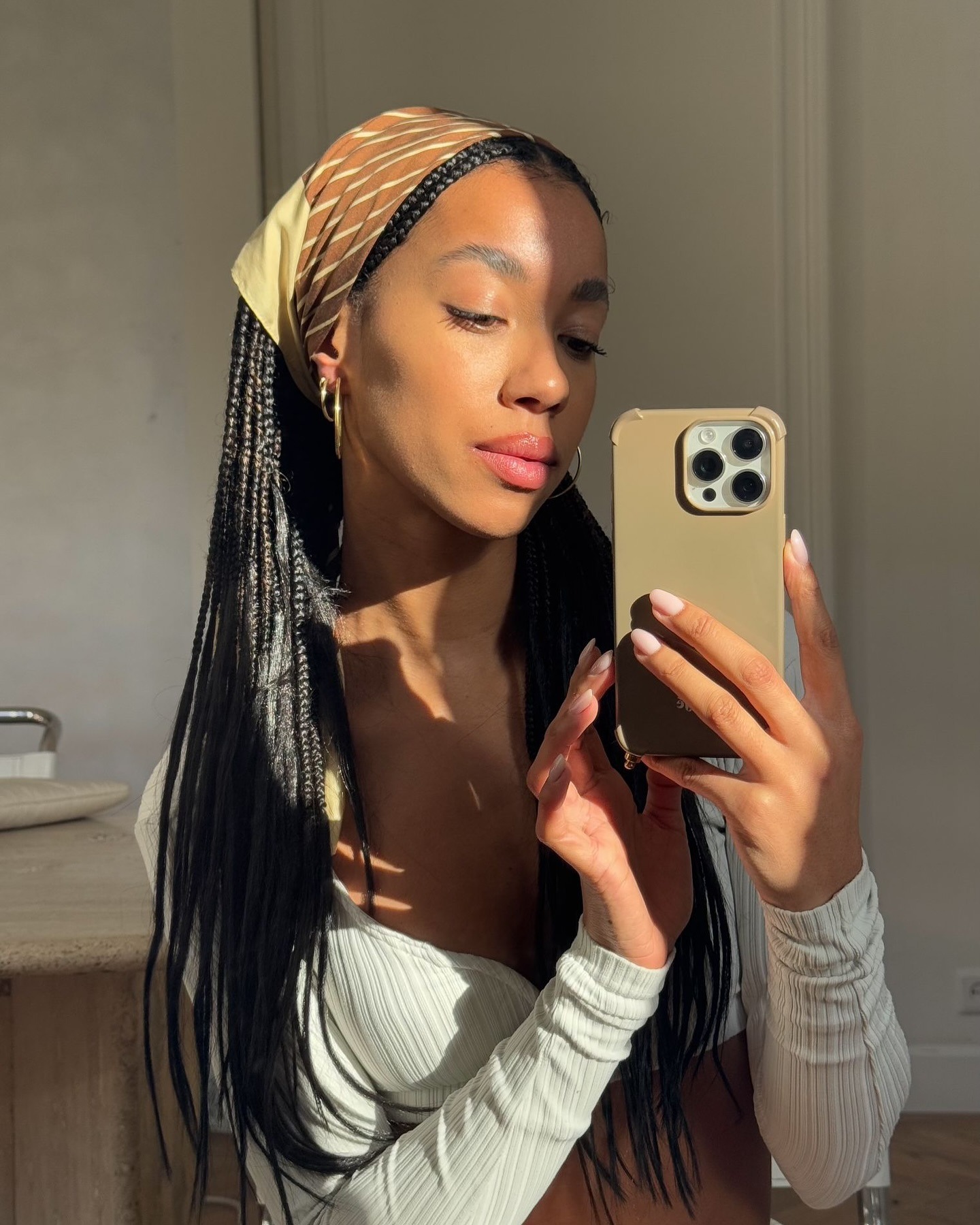 A woman taking a mirror selfie in the sunlight while wearing a headscarf