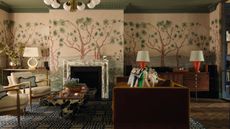 a large London living room with pink and tree motif mural wrapping the walls and chimney breast, a green painted ceiling, marble fireplace and eclectic furniture around a toffee coloured velvet couch