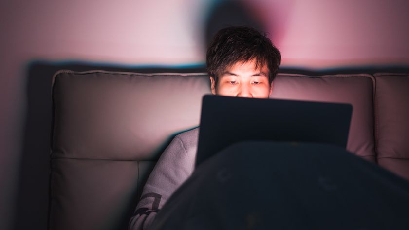 a man sitting up in bed working on a laptop