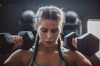 A woman holds a pair of dumbbells at shoulder level