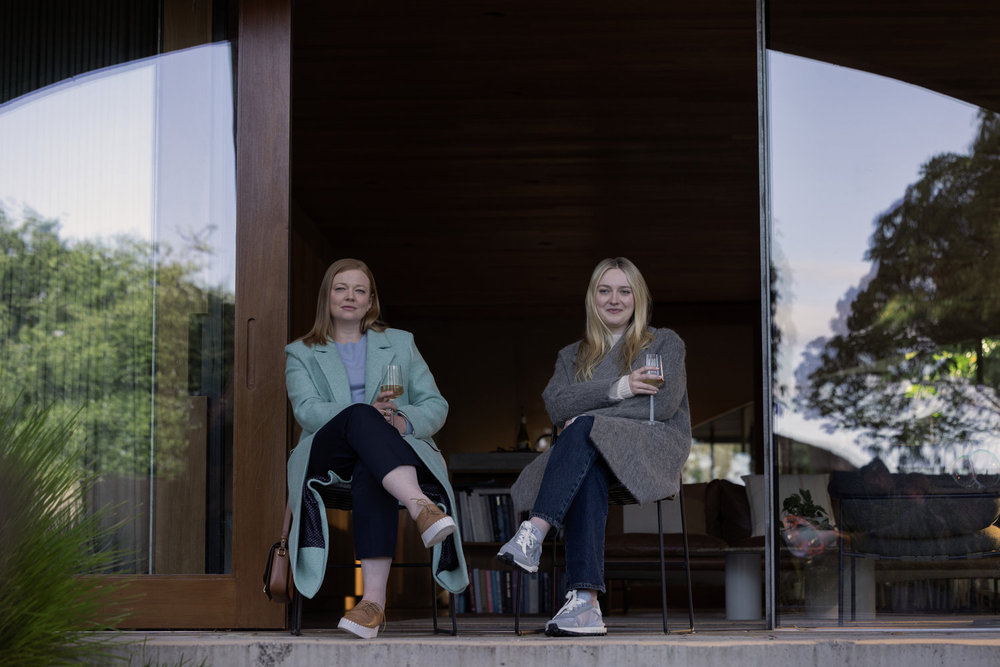 sarah snook as marissa and dakota fanning as jenny sitting on a porch drinking wine in all her fault