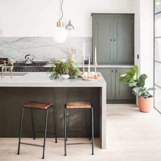 White painted kitchen with sage green cupboards and kitchen island, with a marble splashback behind the hob