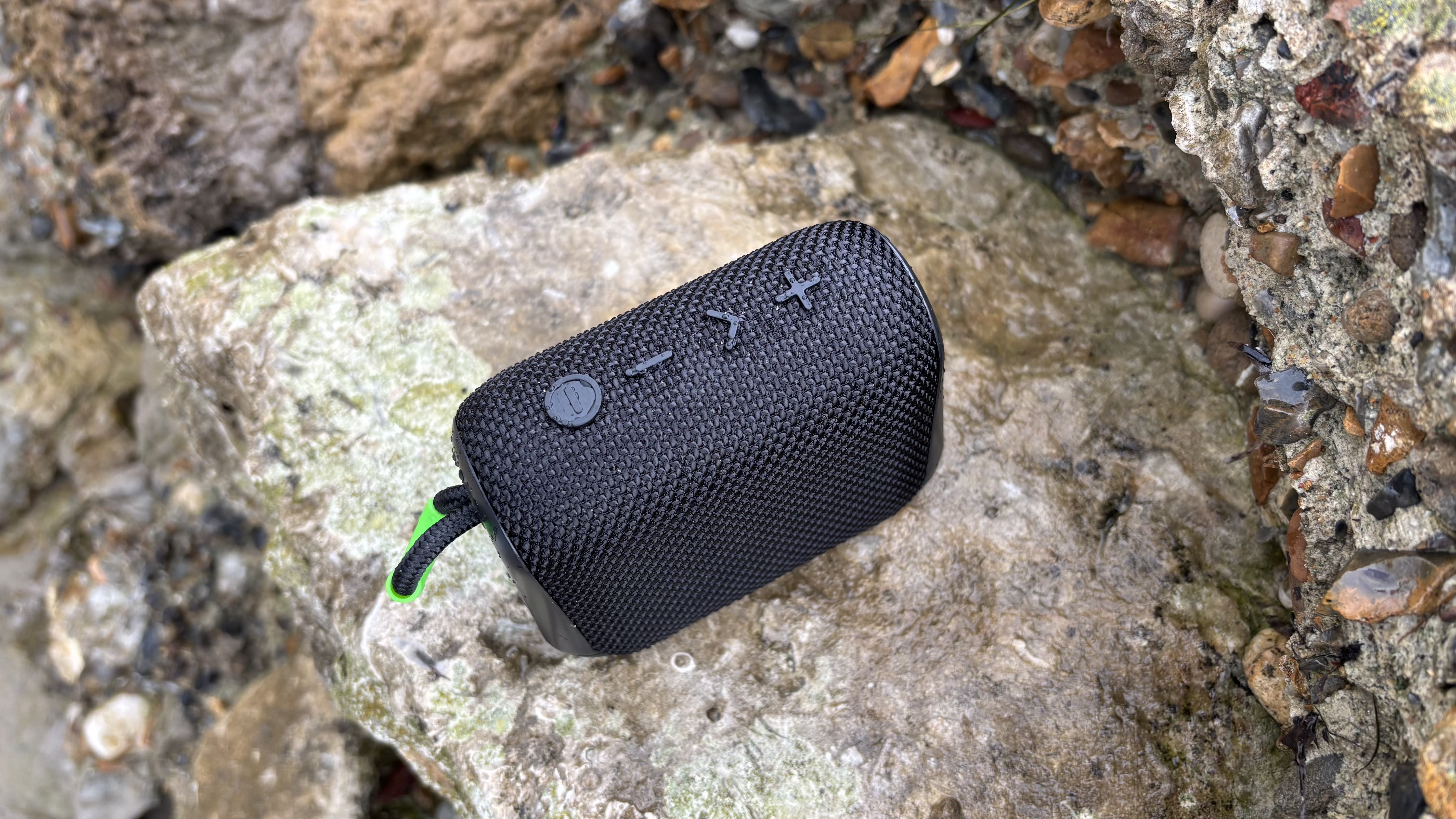 Top panel of the black AO mini portable wireless speaker, on a craggy rock