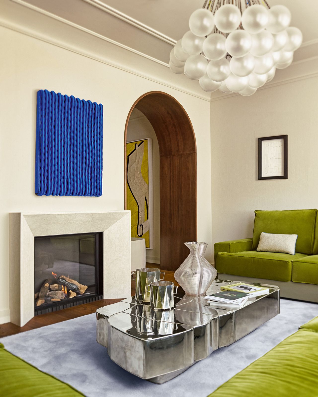 Living room with cream walls, wall-to-wall green velvet corner sofa, chrome coffee table and cobalt blue artwork