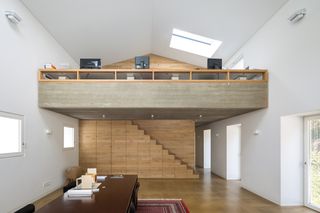 Black Forest House by Stocker Dewes Architekten. A large room with a wooden dining table on a rug, a staircase with a loft above it, three doorways and a skylight.