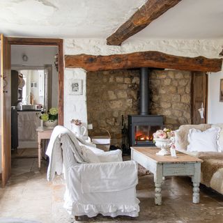 cottage living room with log burner, wooden beams and pale vintage furnishings