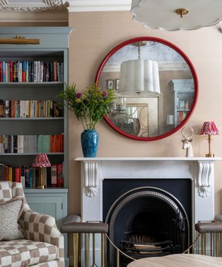 A white fireplace and a circular mirror in a room painted light pink