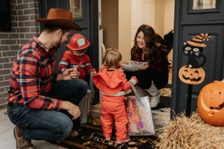 A family dressed up for Halloween trick or treating, collecting sweets from a woman at her door