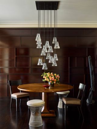 Round dining table in dark wood panelled room with glass multi pendant chandelier
