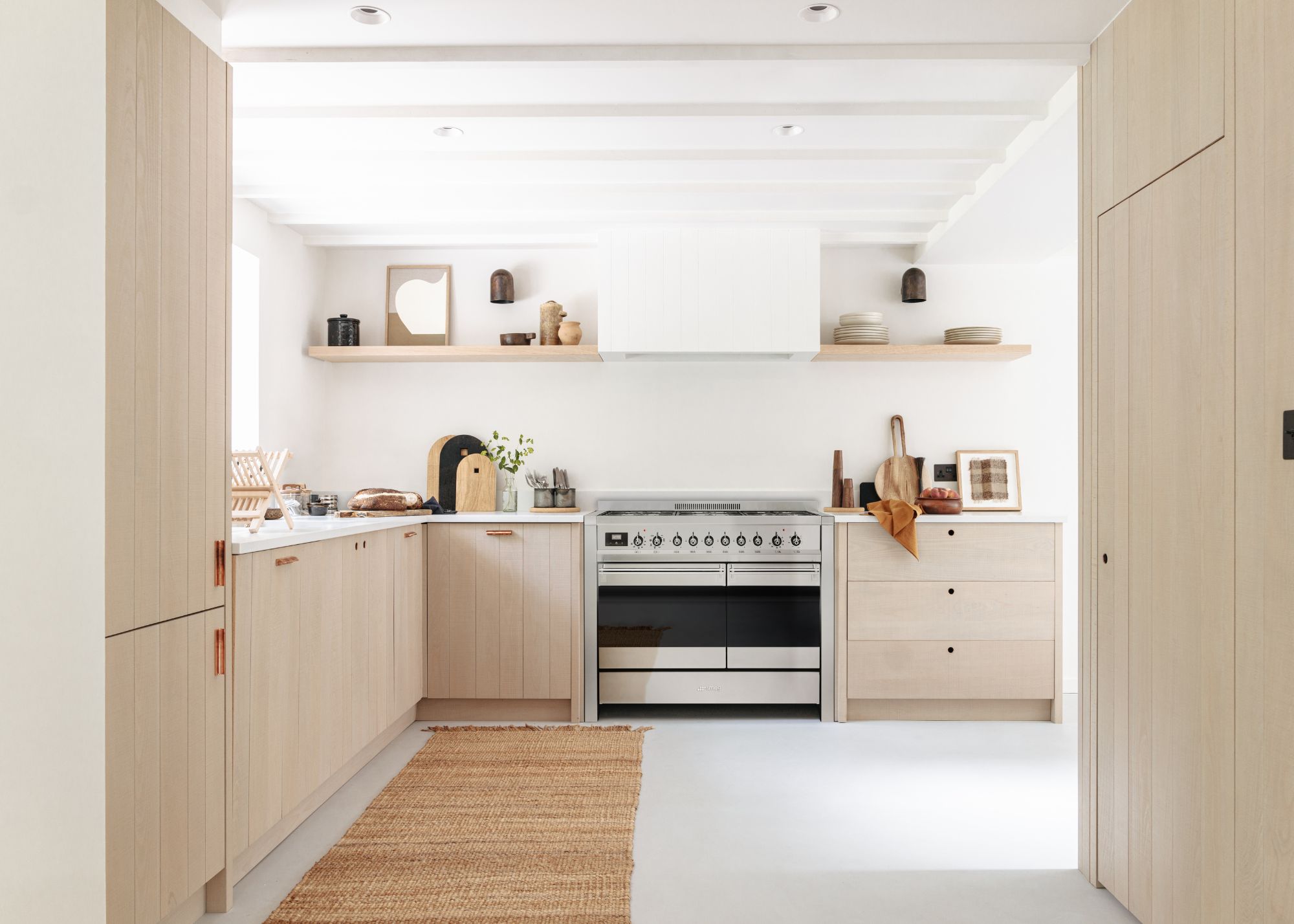 A kitchen with light wood cabinets, a jute runner and a single oven