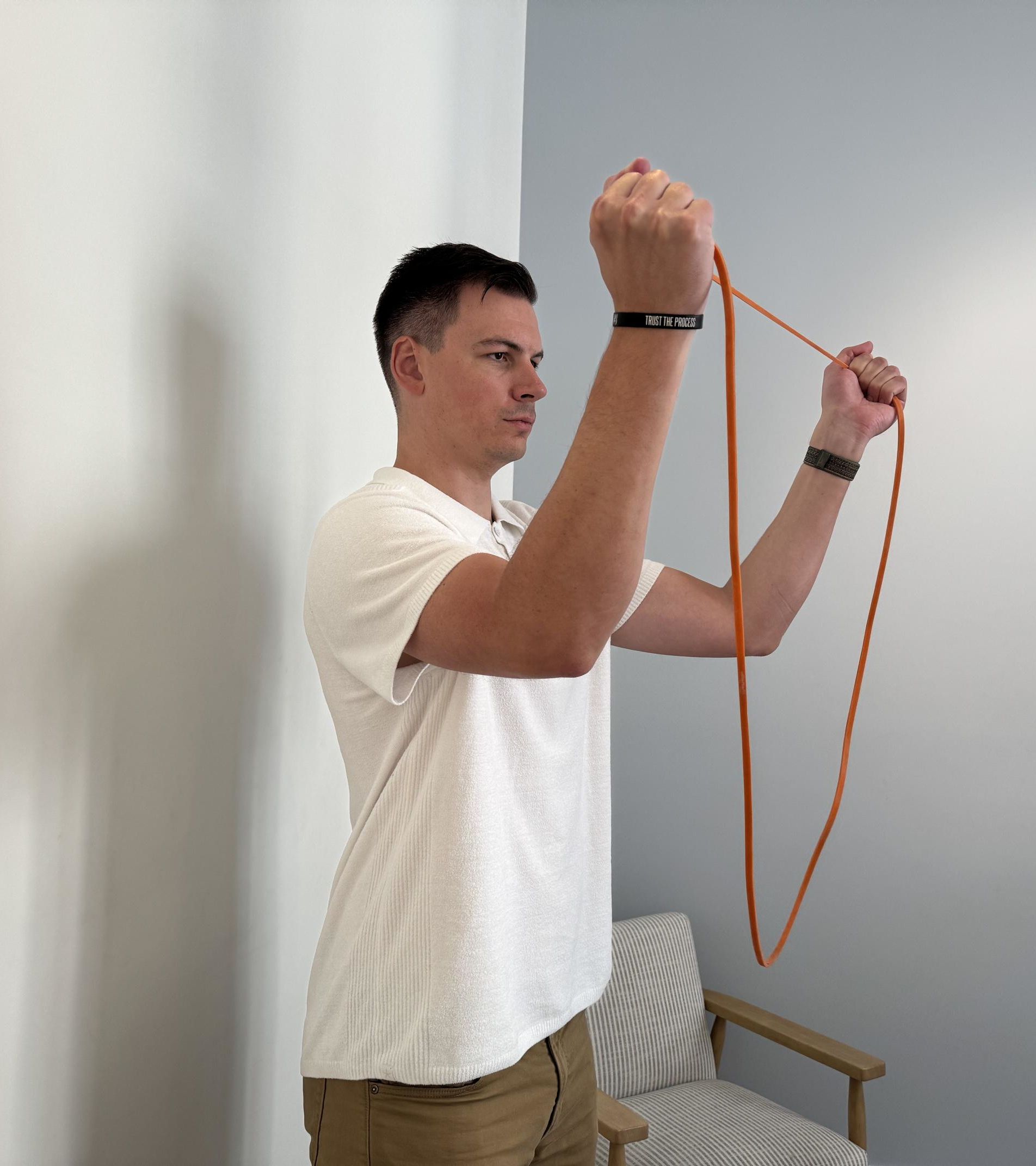 A man holding a thin orange resistance band at head height