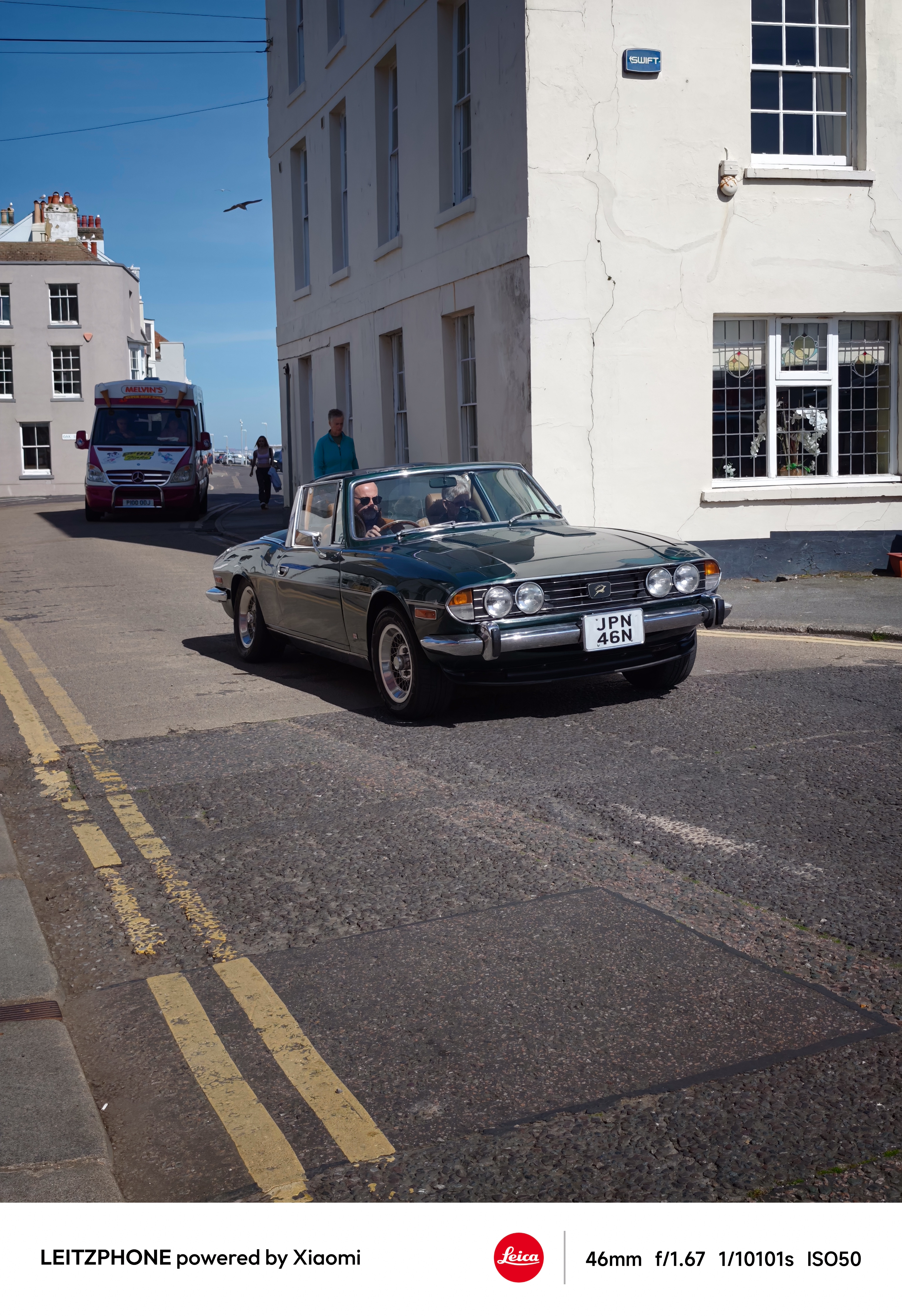 Classic convertible driving down a sunlit street