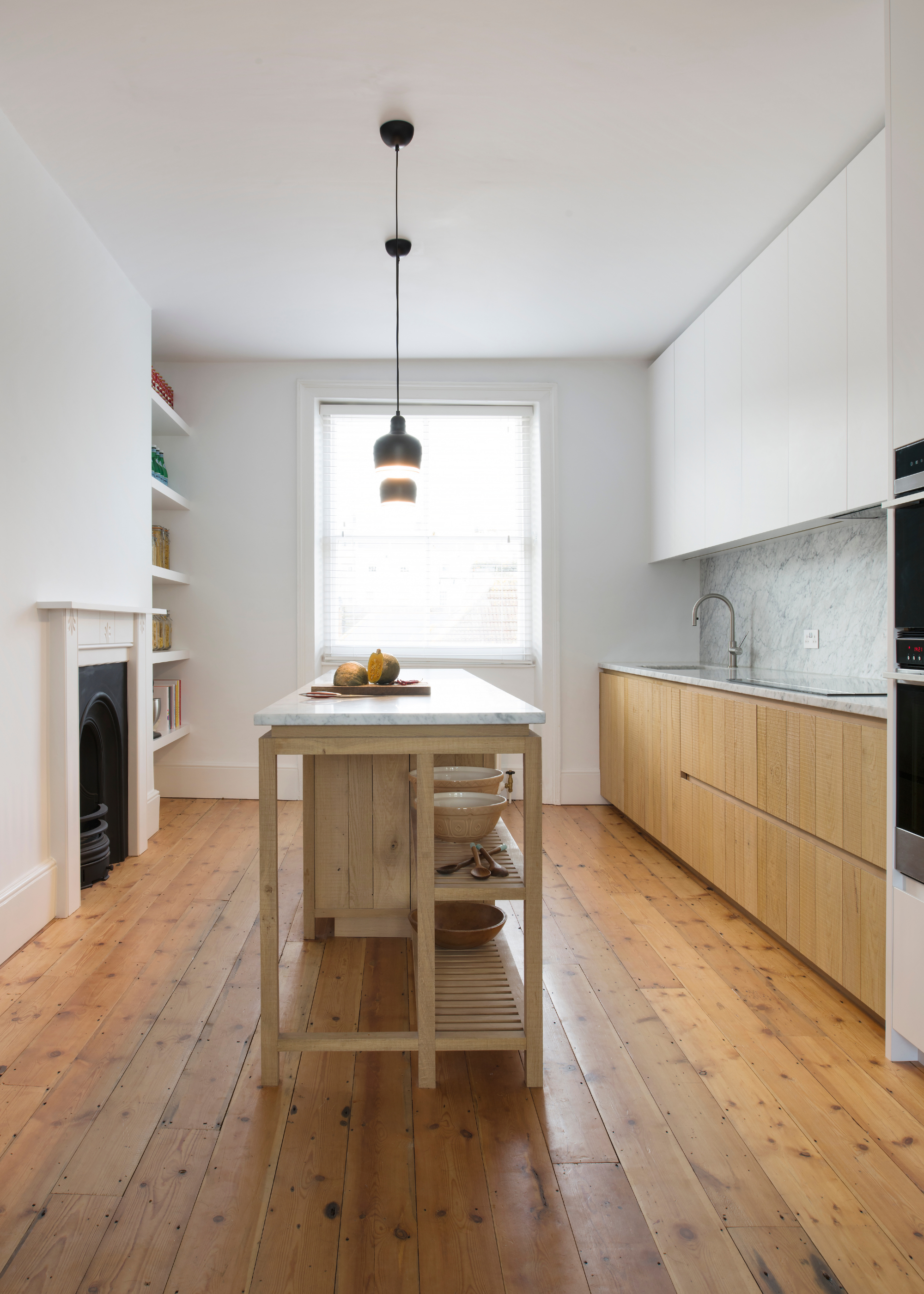 Long narrow kitchen with wooden counters and island, white cabinets and a fireplace in the corner