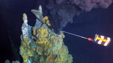 black, mineral-filled water shown spewing out of a hydrothermal vent that a robot is collecting samples from