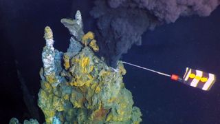 black, mineral-filled water shown spewing out of a hydrothermal vent that a robot is collecting samples from