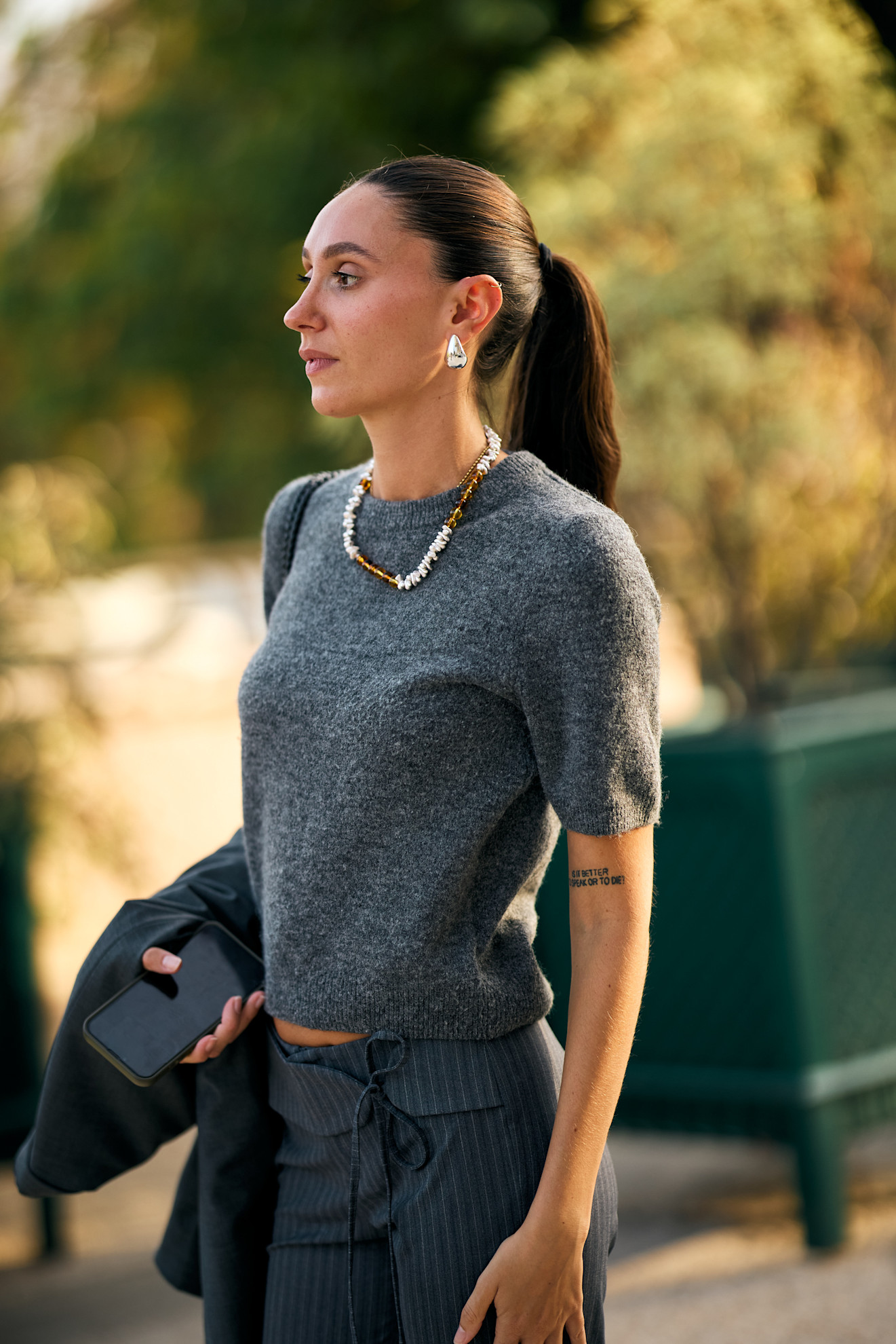 a white woman in a gray short sleeve sweater and red and white necklace with her brown hair in a ponytail