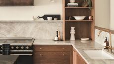 a wood and marble kitchen with open storage, a black stove and a sink with a brass tap