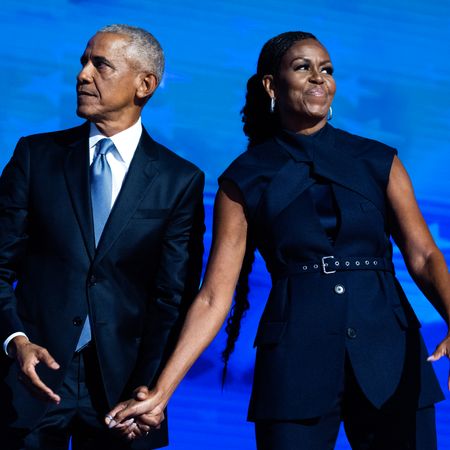 Barack Obama and Michelle Obama hold hands while moving in different directions onstage
