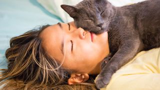 Woman lying on her back on bed cuddling gray cat