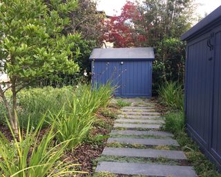 paved garden path leading to a small blue painted bin store