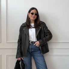 woman wears white tshirt, jeans, leather jcaket, and black handbag along with adidas japan shoes