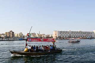 A traditional abra boat filled with people crosses the Dubai Creek on a sunny day