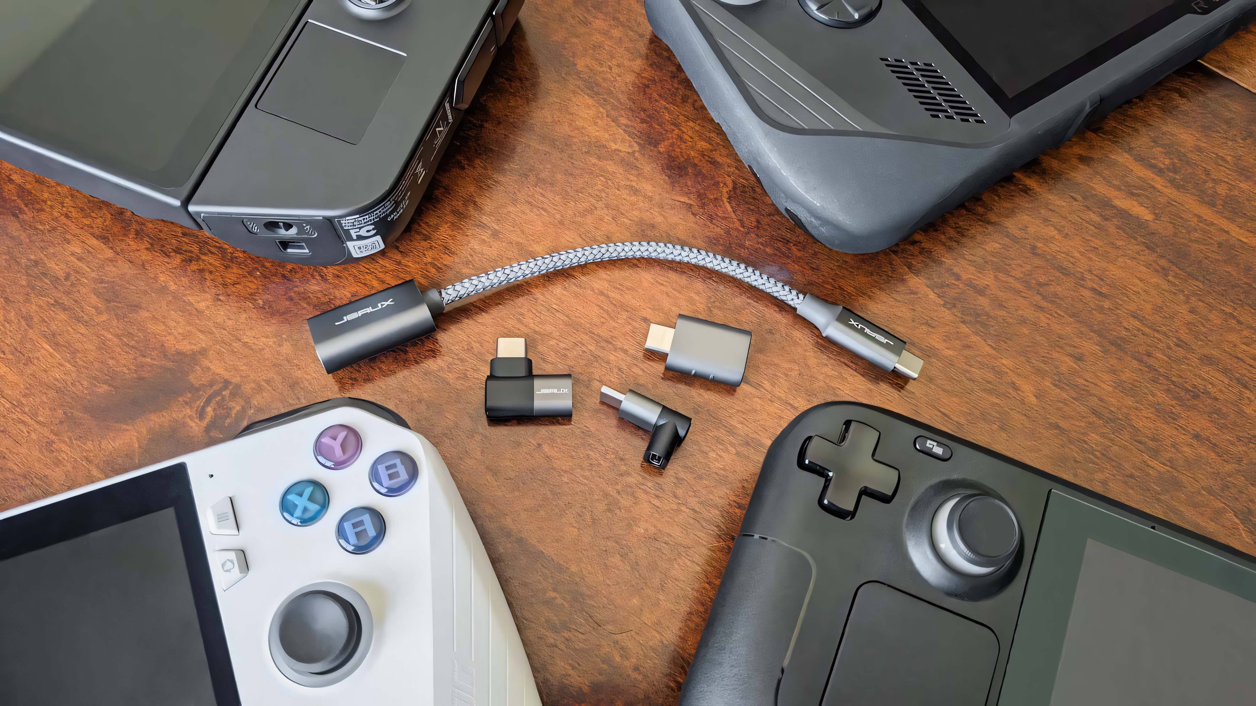 A JSUAX USB-C to USB-C adapter with a cable, a USB-C to USB-A adapter, and two USB-C 90-degree adapters surrounded by a Steam Deck, ROG Ally, Ally X, and Legion Go.