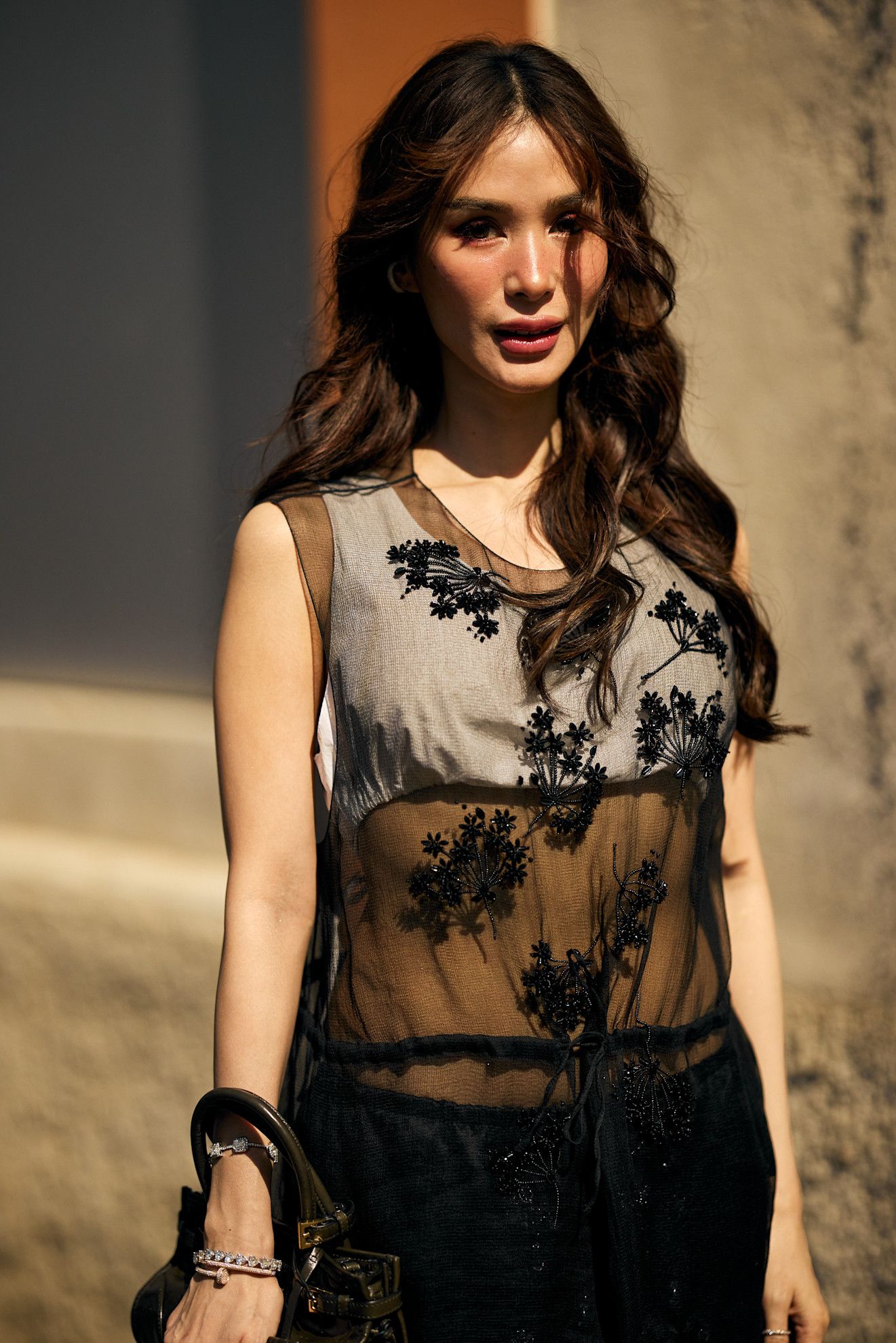 an older asian woman in a sheer black dress with wavy brown hair