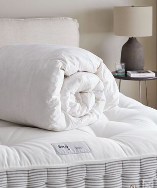 Rolled comforter on mattress on bed in room with night table and lamp