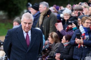 Prince Andrew wearing a coat and red tie standing in front of a crowd of people in coats and scarves on Christmas Day