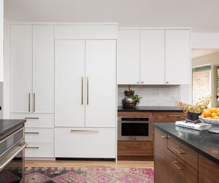 White and wooden kitchen cabinets are paired with a pink patterned runner, colorful fruit bowls, and pink flowers.