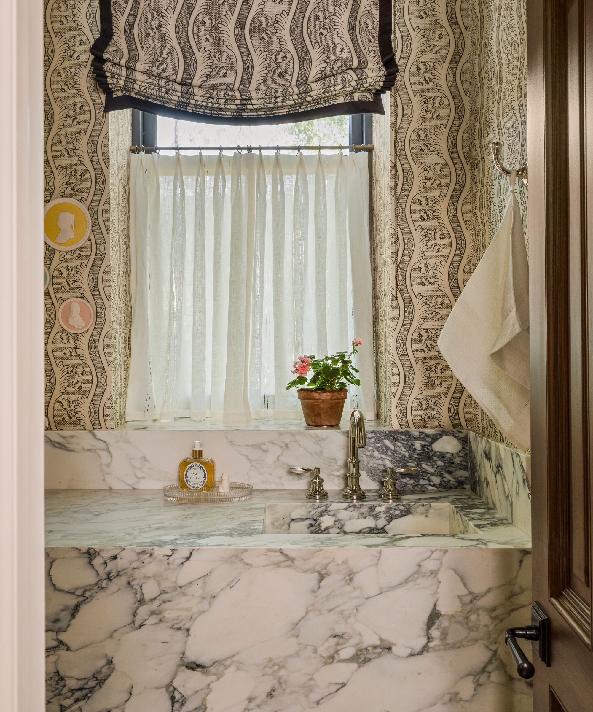 a pattern drenched powder room with matching wallpaper and window blind with a large marble vanity