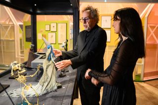 Tim Burton handles some of the models of his spooky characters in a museum setting lit up in warm lights.