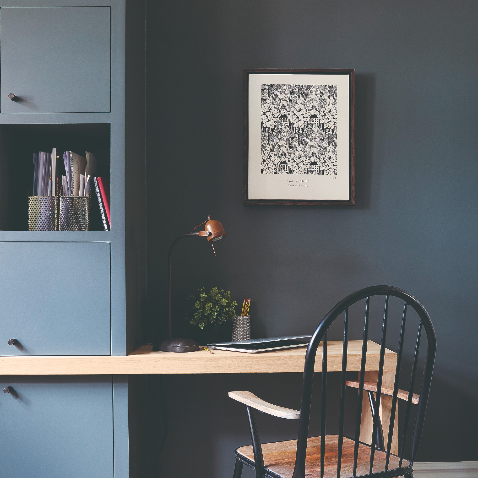 A dark painted home office with a desk and a print on the wall