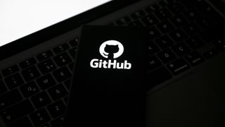 GitHub logo and branding displayed on a smartphone screen placed on top of a laptop keyboard.