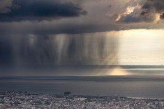 Rain shaft with dramatic thunder cloud at sunset and rays of light over the Gulf of Patras, Greece.