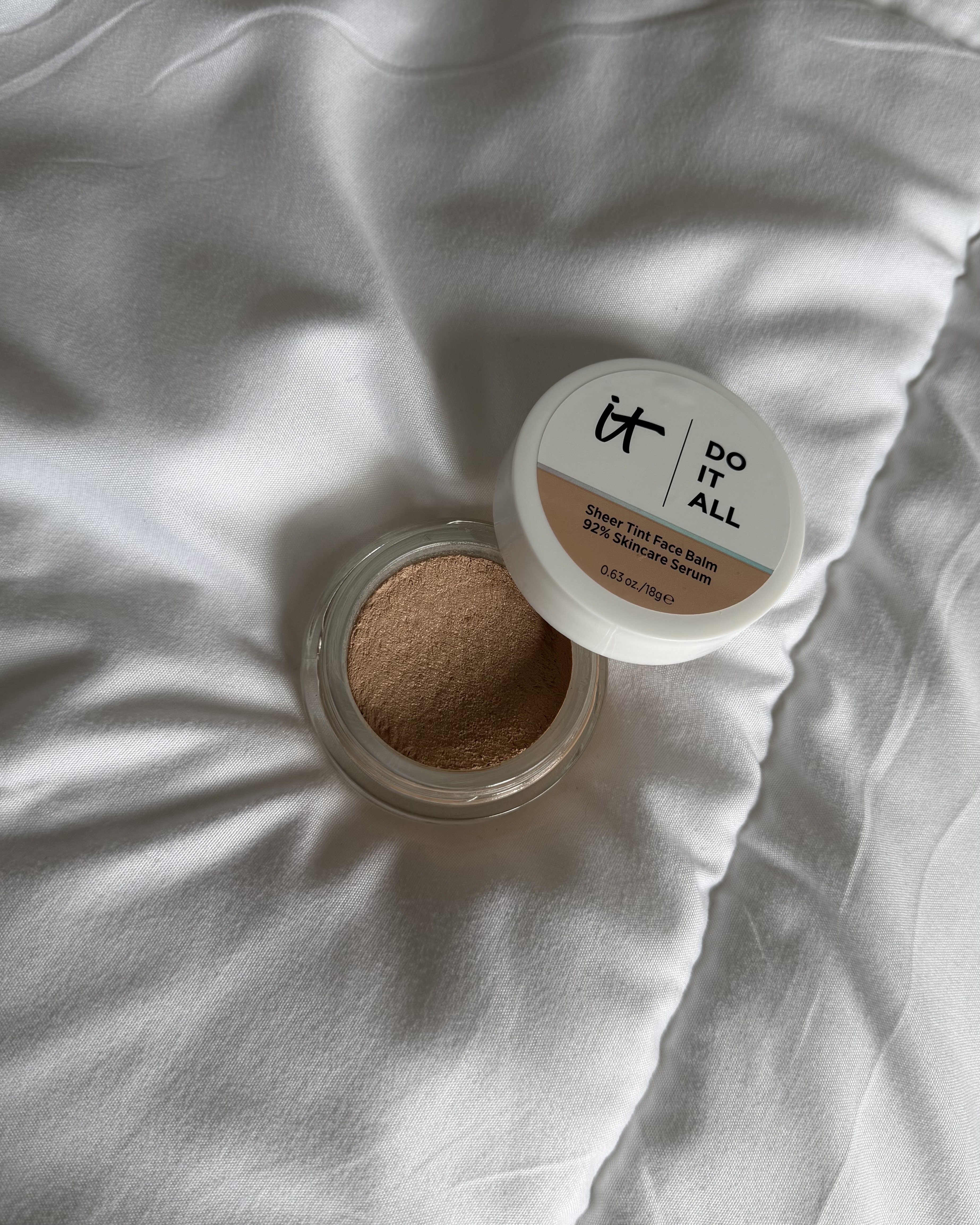 An image of the It Cosmetics Do It All Sheer Tint Face Balm on a bedspread.