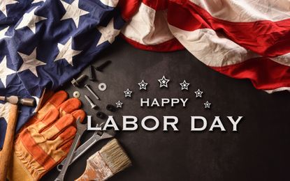 Happy Labor Day written in white letters next to construction equipment and american flag