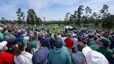 Patrons stand around a player hitting a shot at the Masters par 3 contest