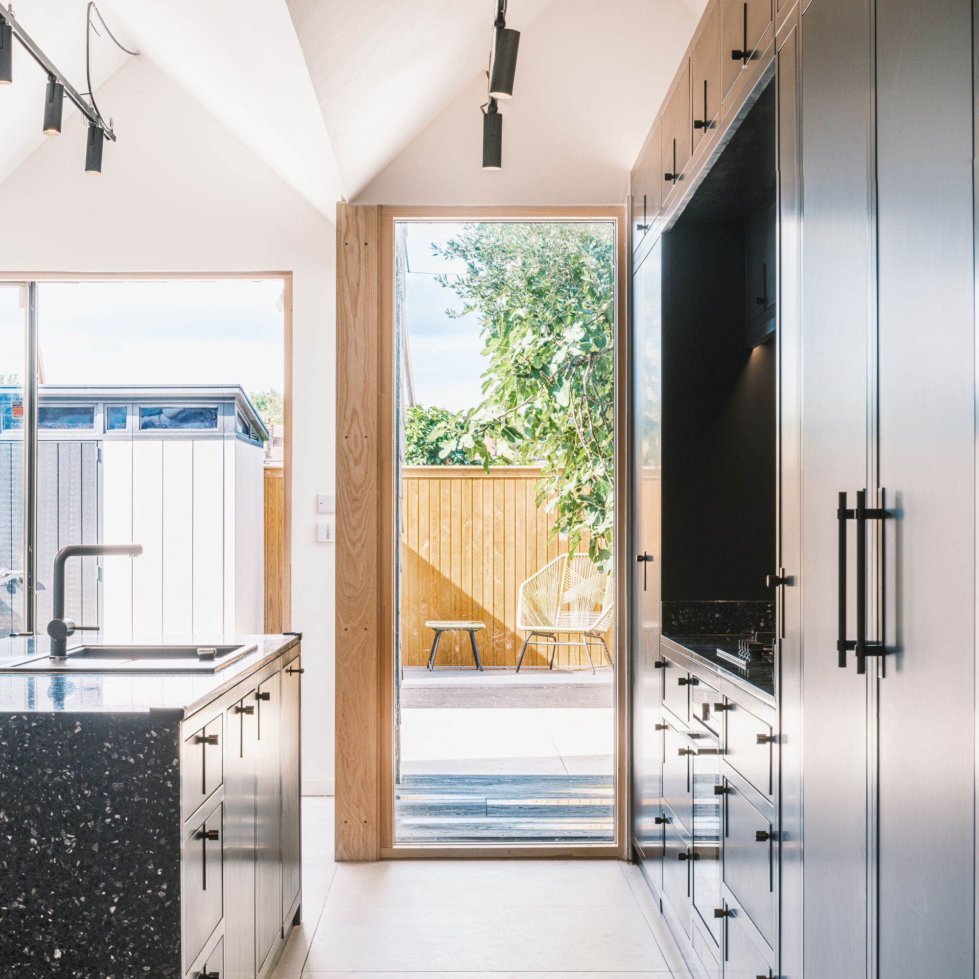 a galley kitchen with black cabinets and floor to ceiling glazing