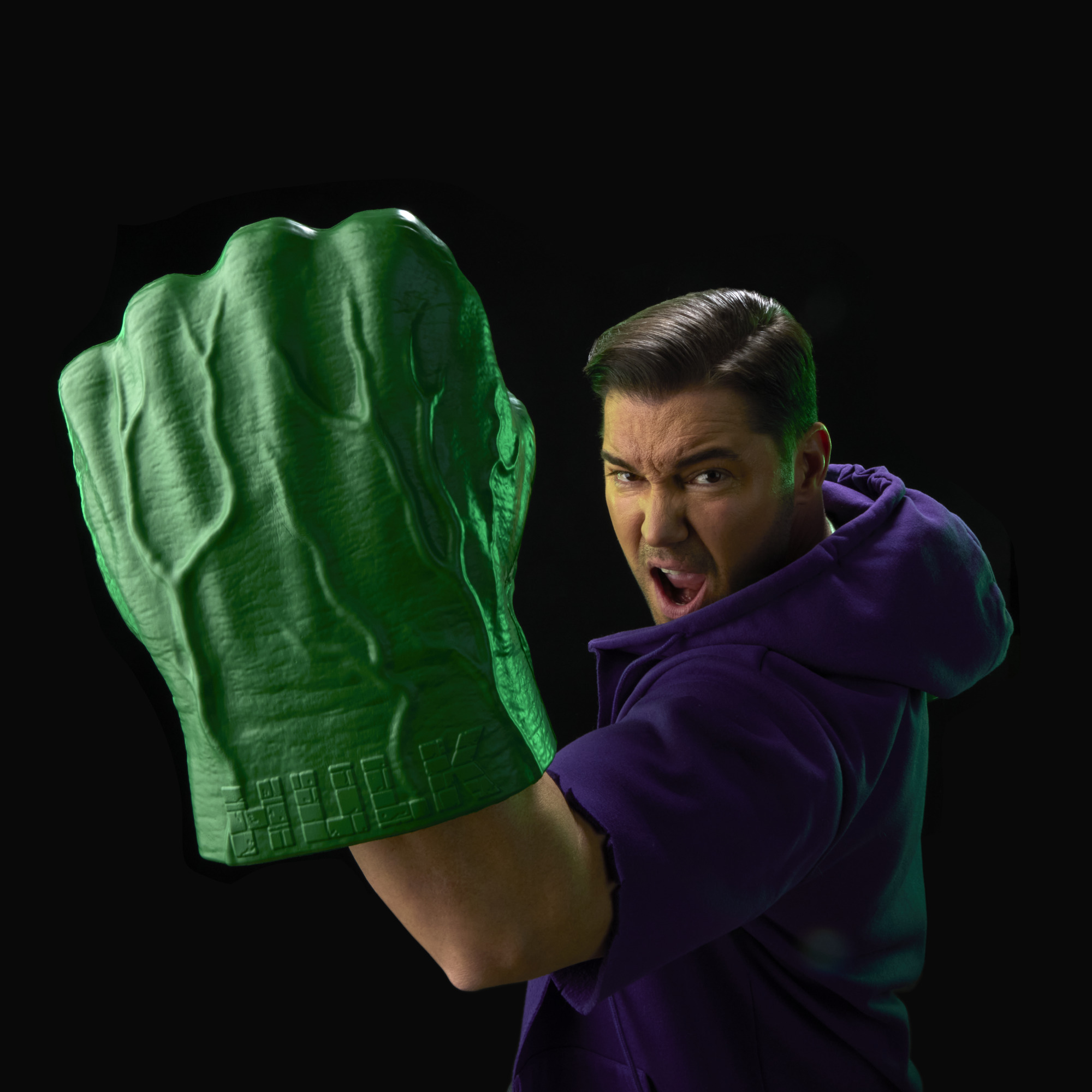 A roaring man with two Hulk Fists pretends to punch with them against a black background
