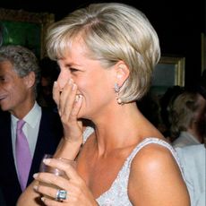 Princess Diana covering her mouth and laughing while holding a wine glass and wearing a beaded blue dress