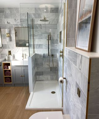 their gray tiled bathroom with gold hardware and a wooden floor