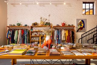 A sun-lit, colorfully decorated industrial-style store features a multidisciplinary selection of printed matter, clothing, wall art, and homewares.